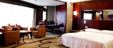 A hotel room with a large bed, two armchairs, a desk, and a large mirror.