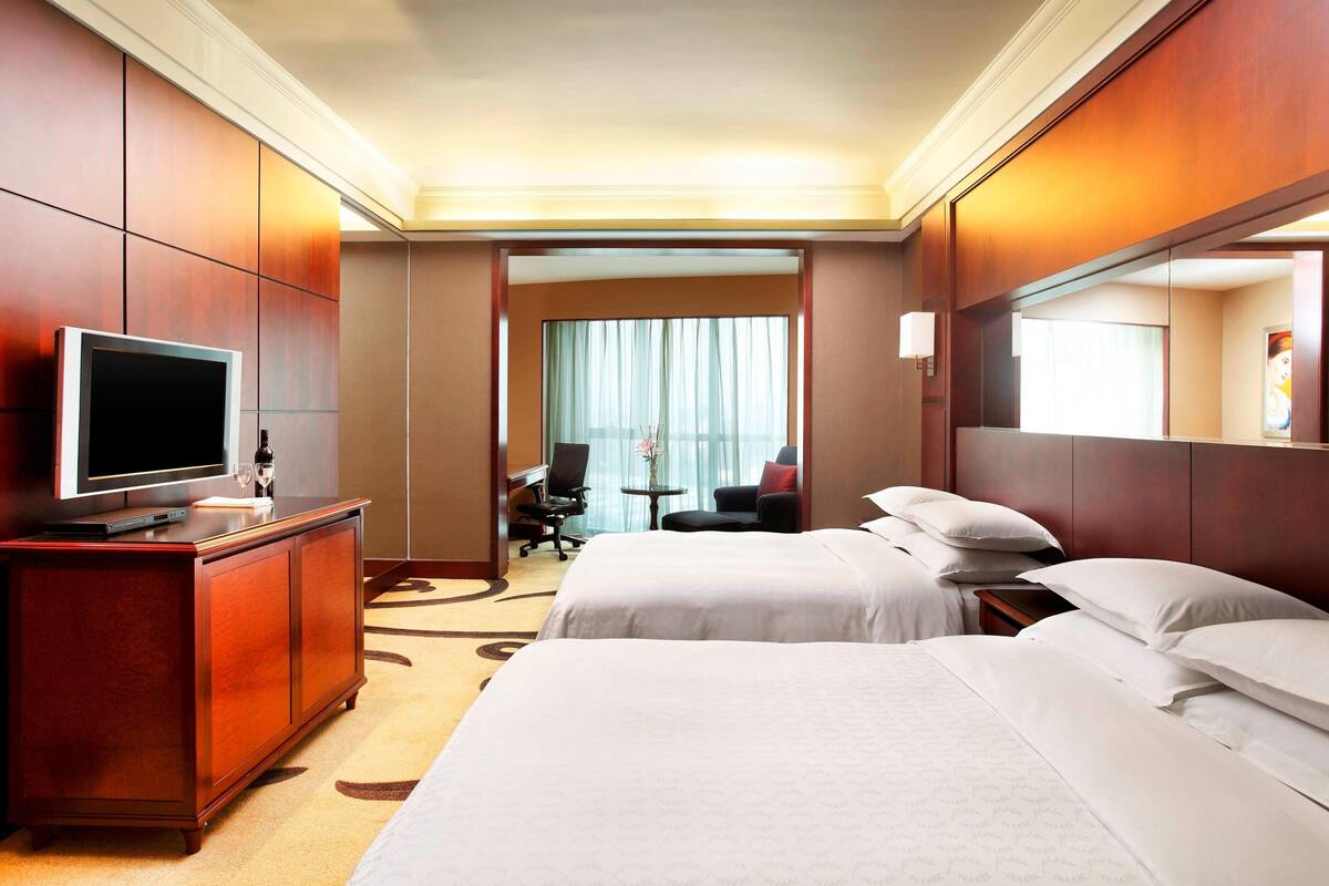 Ein Hotelzimmer mit zwei Betten, einem Fernseher, einem Schreibtisch und einem Stuhl.