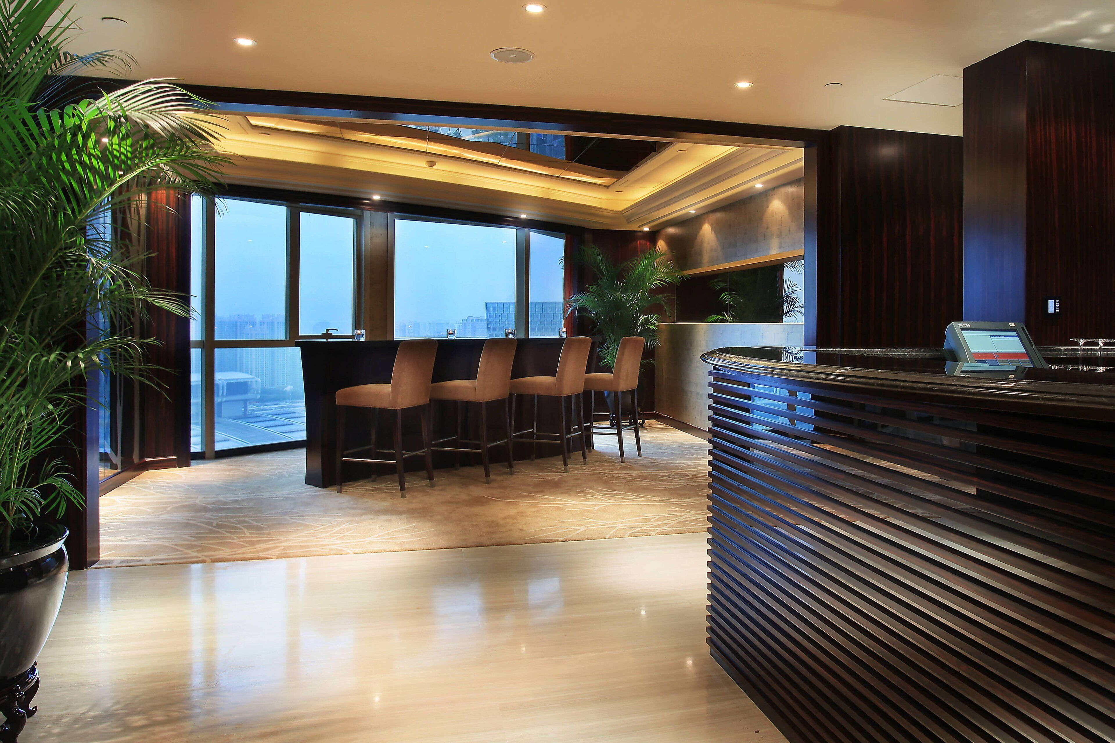 Un área de recepción moderna con bar, asientos y ventanas amplias que ofrecen vista a la ciudad.