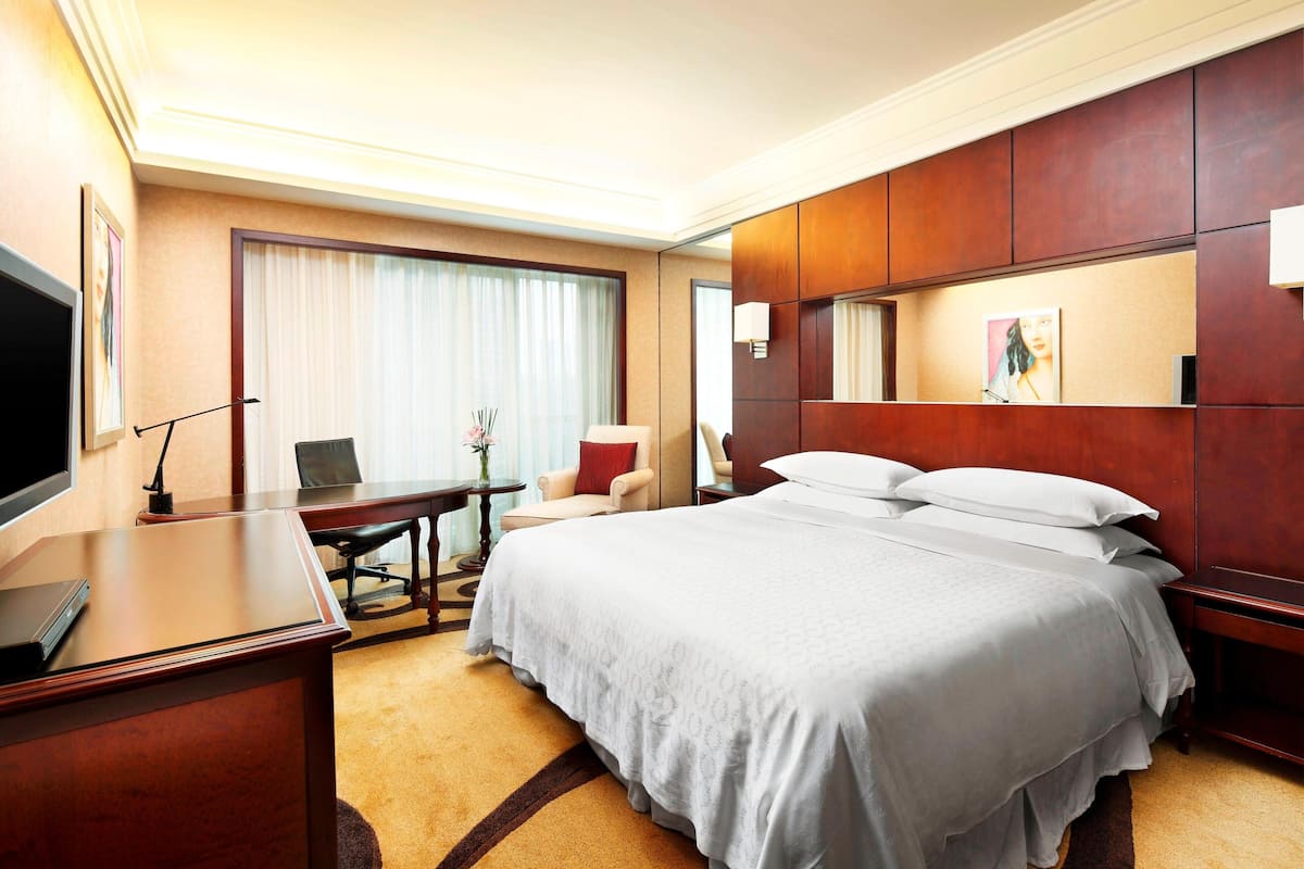 Ein Hotelzimmer mit einem großen Bett, einem Schreibtisch mit Computer, einem Sessel und einem Fernseher.