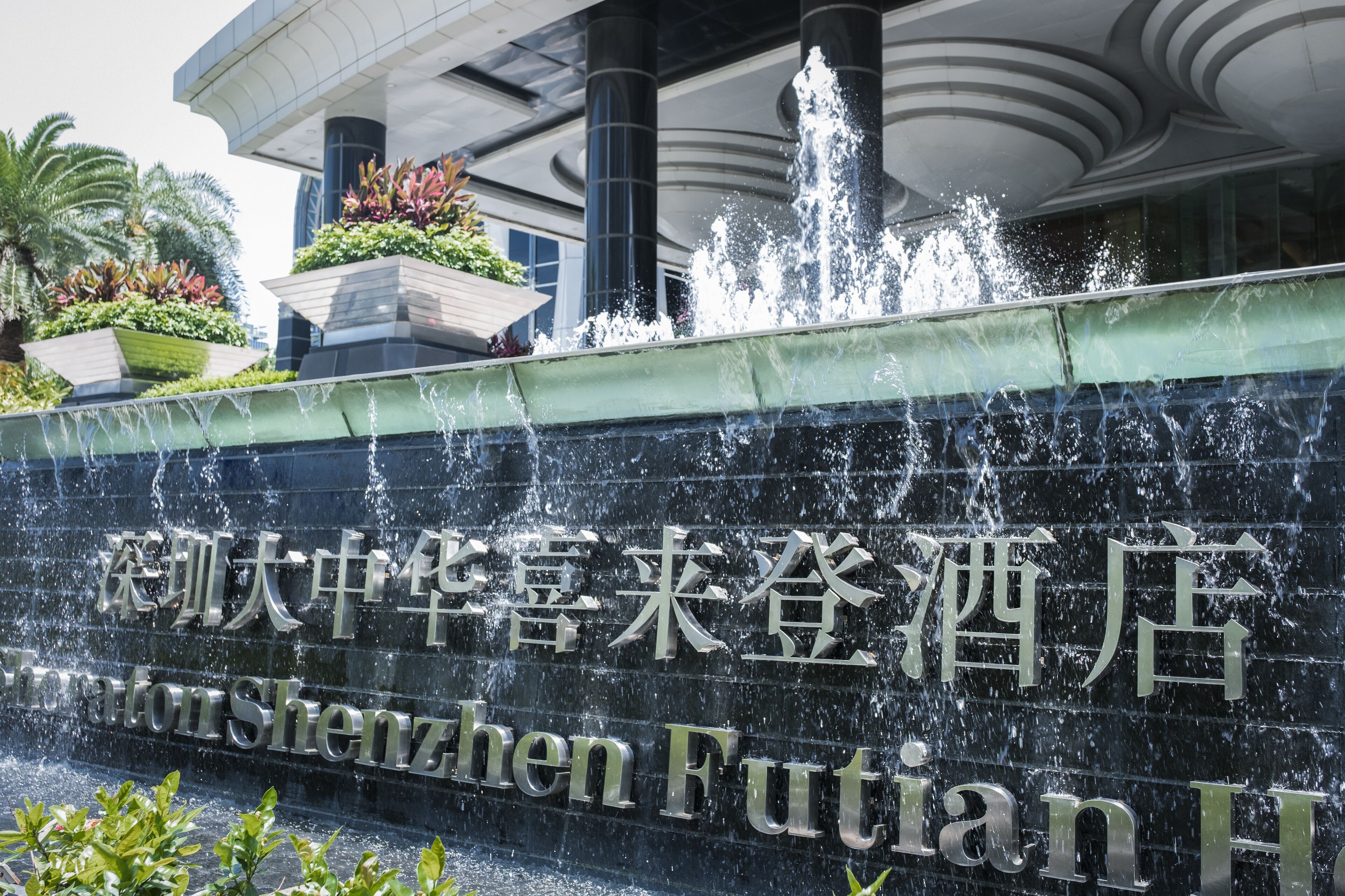 A hotel entrance with a water feature and a sign in both Chinese and English.