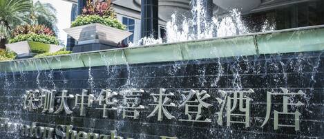 A hotel entrance with a water feature and a sign in both Chinese and English.