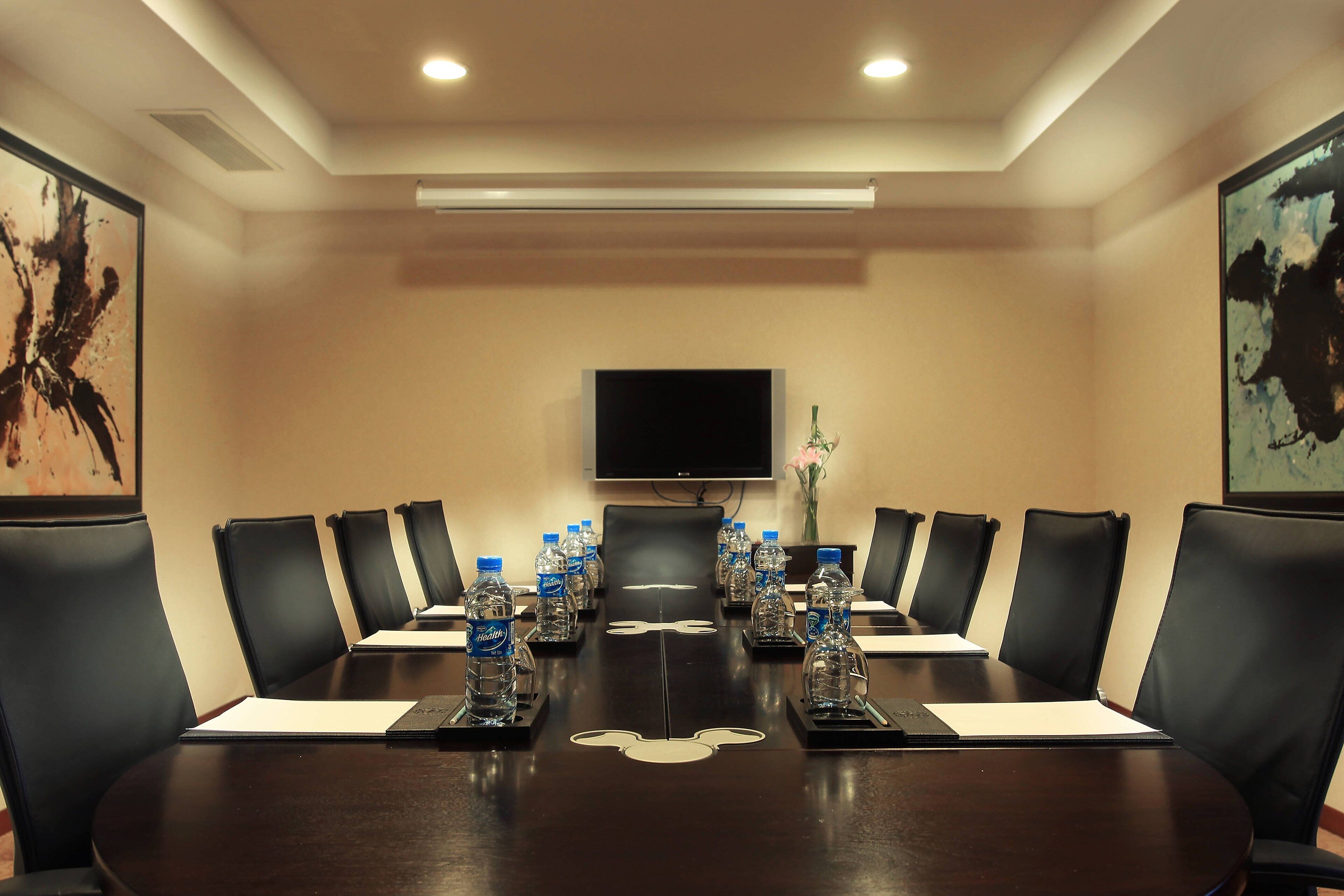 Una sala de conferencias con una mesa de madera oscura, sillas de cuero negro, botellas de agua y un televisor de pantalla plana en la pared.