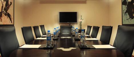 Una sala de conferencias con una mesa de madera oscura, sillas de cuero negro, botellas de agua y un televisor de pantalla plana en la pared.