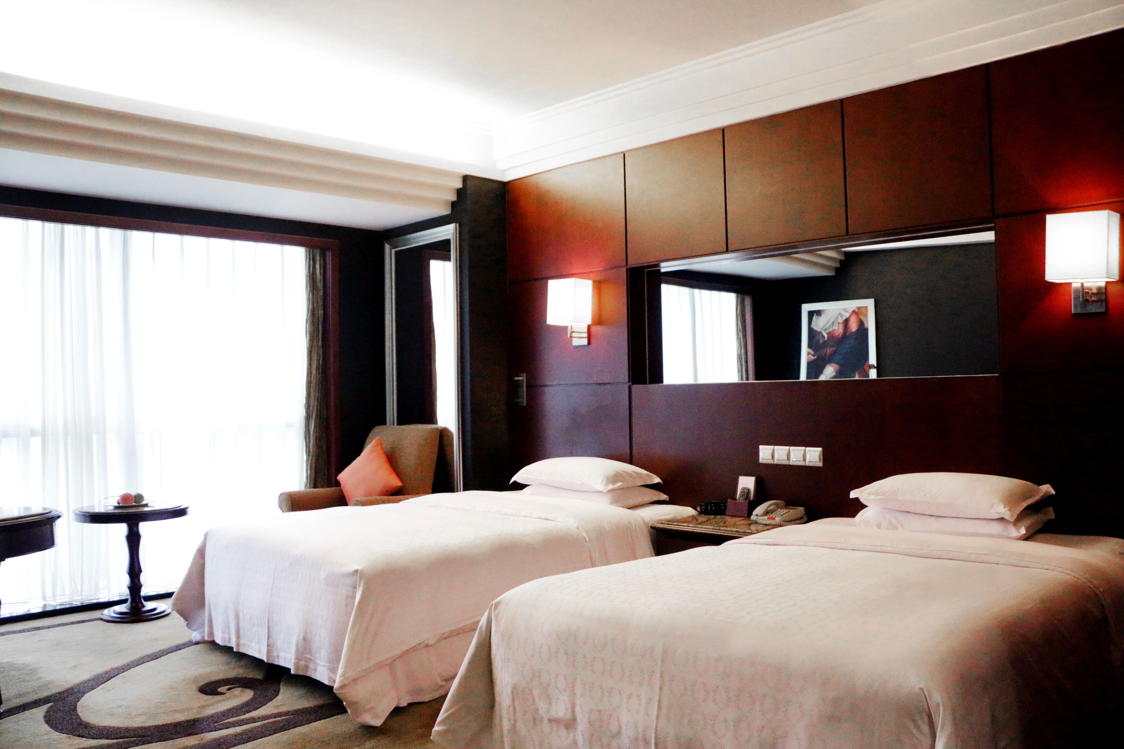 Habitación de hotel con dos camas, una silla, una mesita pequeña y una mesita de noche con un teléfono.