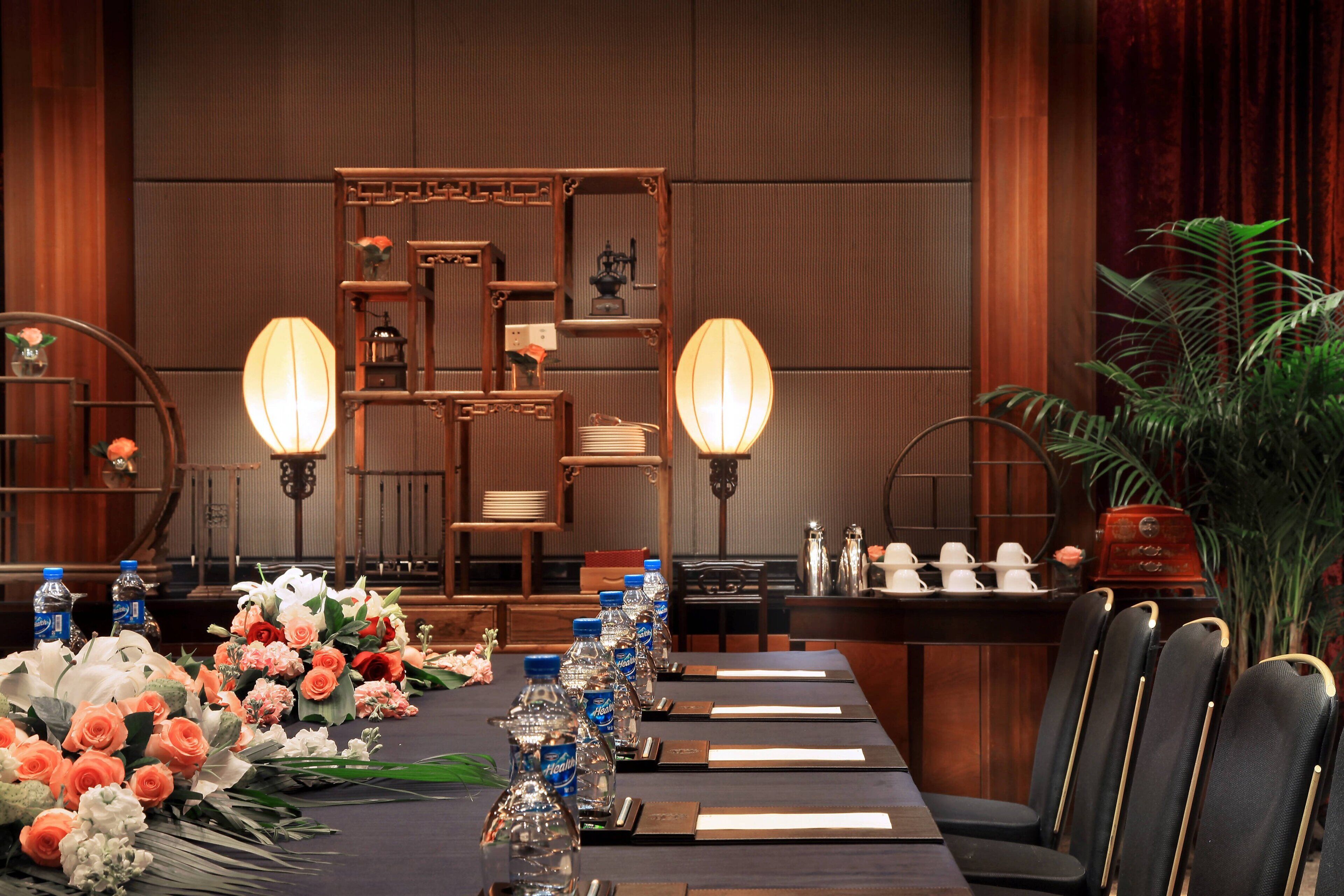 A formal dining table set with floral arrangements, water bottles, and place settings in a room with wooden paneling and traditional decor.