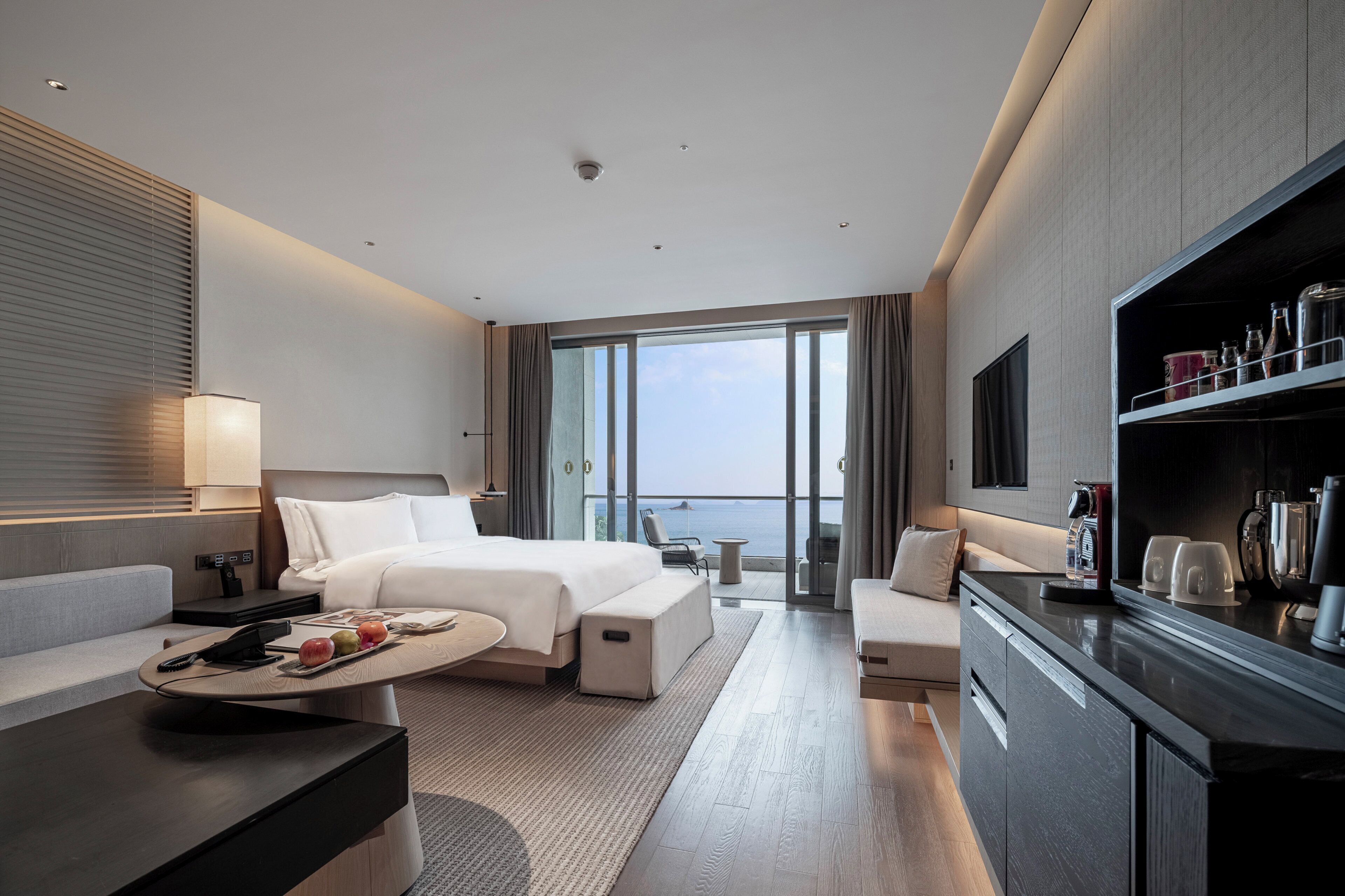 A modern hotel room with a bed, seating area, and a view of the sea.