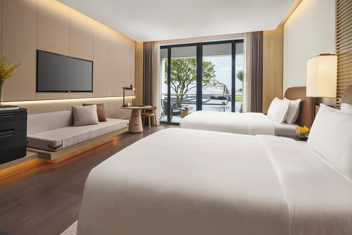 Una habitación de hotel moderna con dos camas, un televisor de pantalla plana, un sofá y un balcón con vista al agua.
