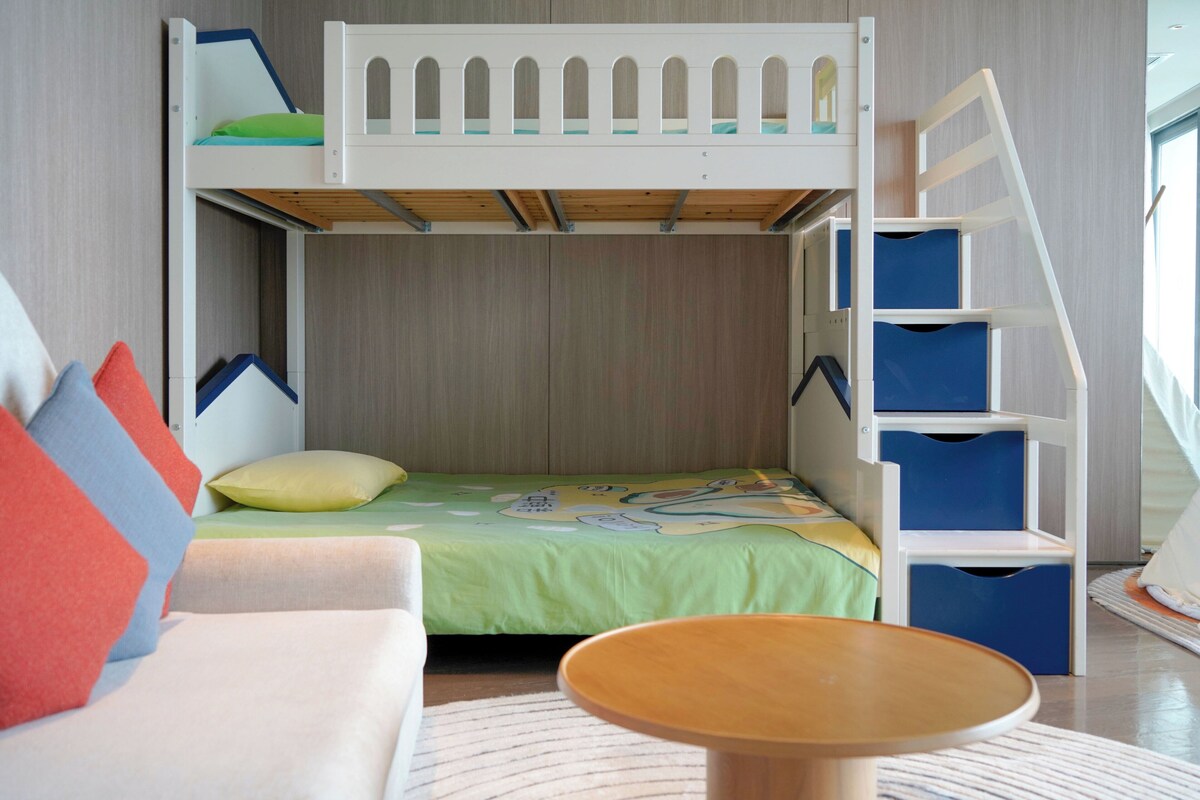 Una cama en literas con escalera, una mesita pequeña y un sofá en una habitación con paredes de madera.