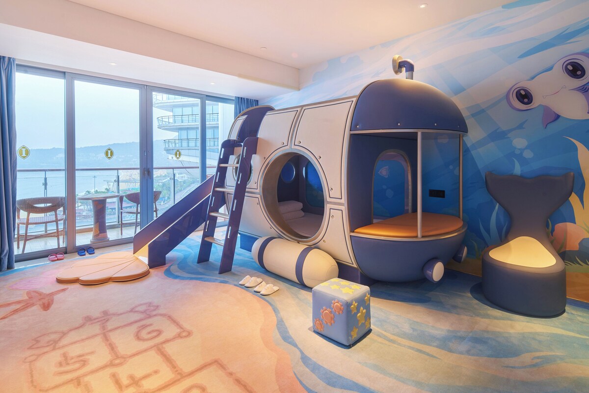 Zona de juegos infantiles con un tobogán, una casita de juegos y vistas al mar.
