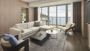 A modern living room with a large sofa, a coffee table, and a chair. There is a large window with a view of the sea and buildings. - InterContinental Shenzhen Dameisha Resort by IHG (Shenzhen)