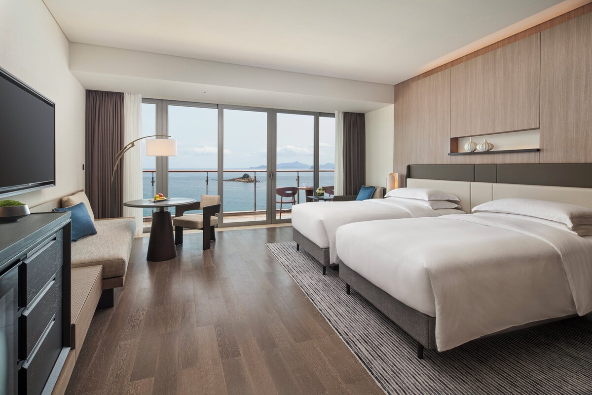Una habitación de hotel moderna con un balcón grande, un sofá, un escritorio y dos camas.