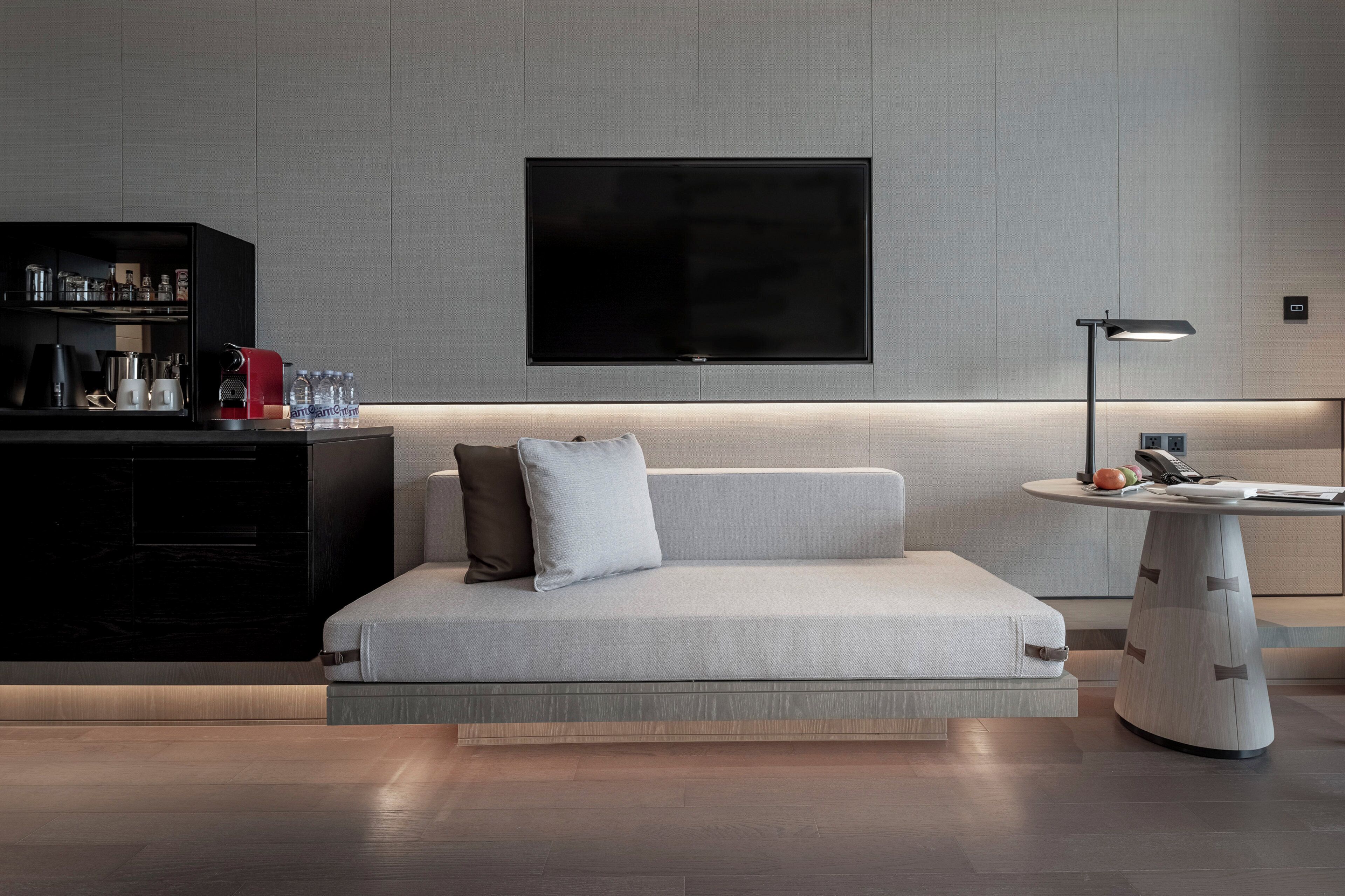 A modern living room with a sofa, a coffee machine, and a flat-screen TV mounted on the wall.