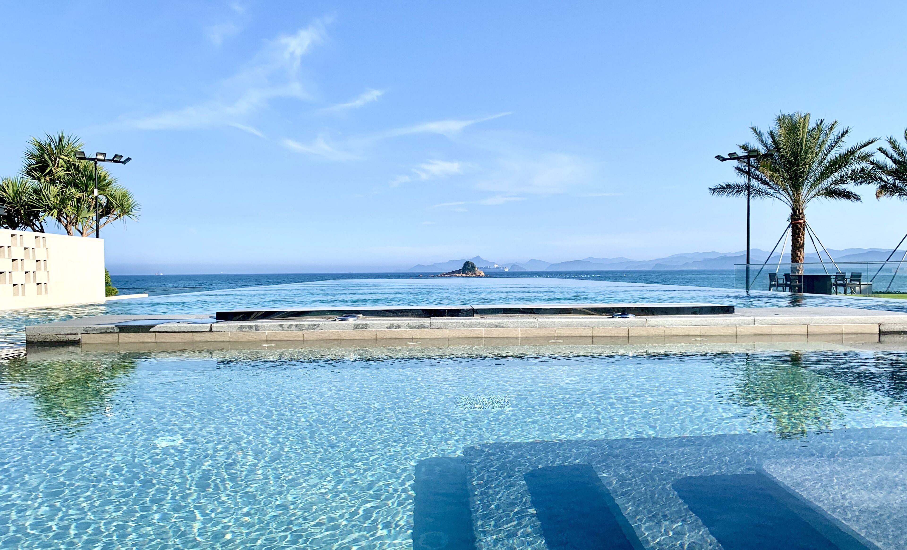 A clear pool with a view of the sea and mountains in the background.