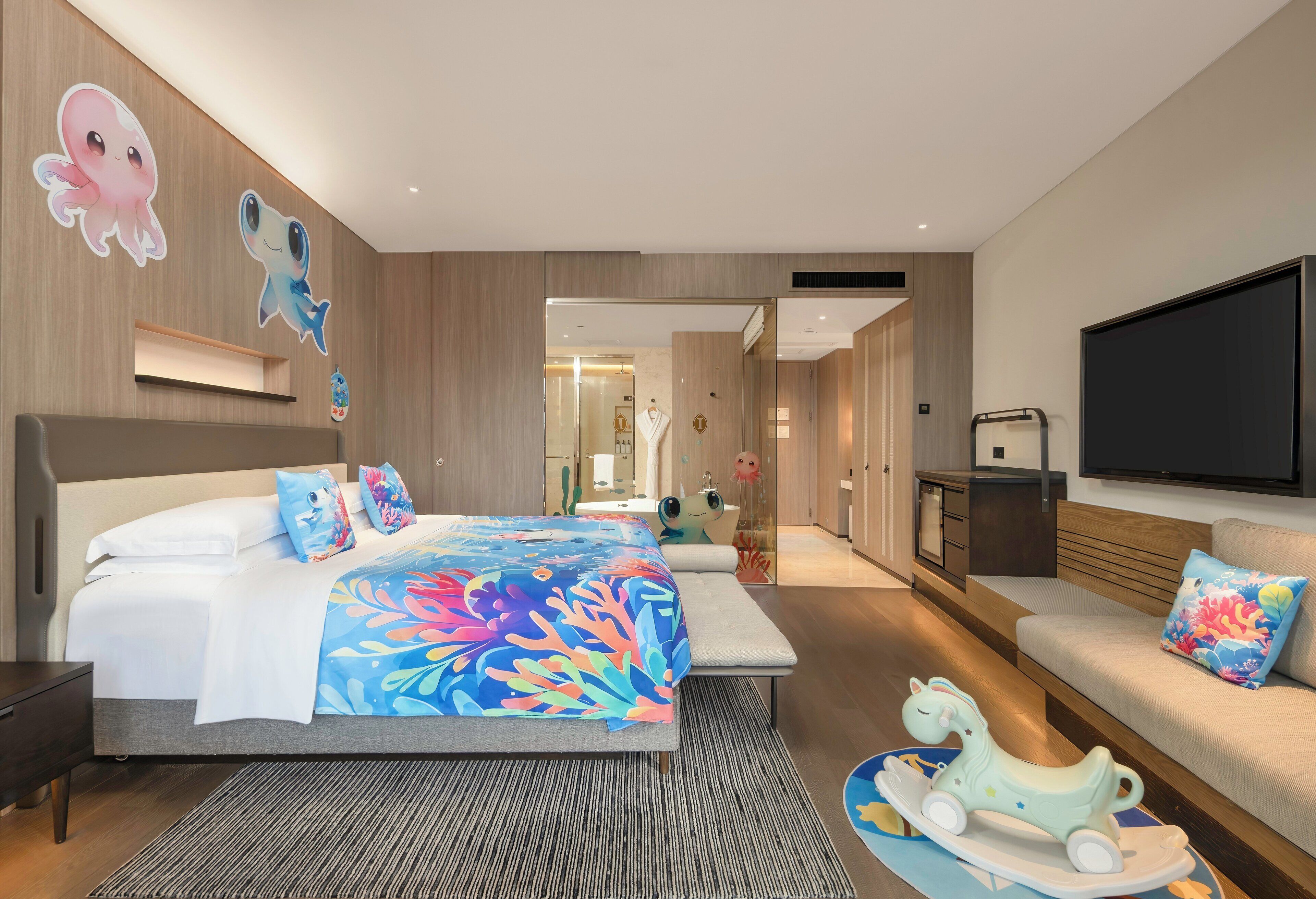 A modern hotel room with a large bed, a sofa, a TV, and a bathroom visible through an open door.