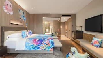 A modern hotel room with a large bed, a sofa, a TV, and a bathroom visible through an open door.