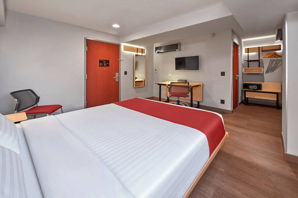 A hotel room with a large bed, a desk, a chair, a TV, and a wardrobe.