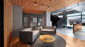 Un vestíbulo moderno con un sofá, sillones, una mesa de centro redonda, suelo de madera y una escalera que conduce a un nivel superior.