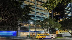 Un edificio moderno con fachada azul, una furgoneta amarilla estacionada adelante y un letrero iluminado grande.