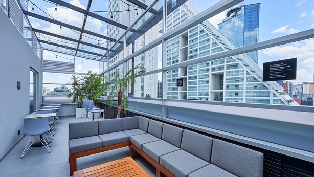 Un lounge moderno en la azotea con una mesa de madera, asientos acolchados grises y vistas de edificios de la ciudad.