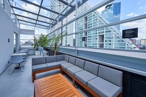 A modern rooftop lounge with a wooden table, grey cushioned seating, and a view of city buildings. - City Express by Marriott Ciudad de México EBC Reforma (Mexico City)