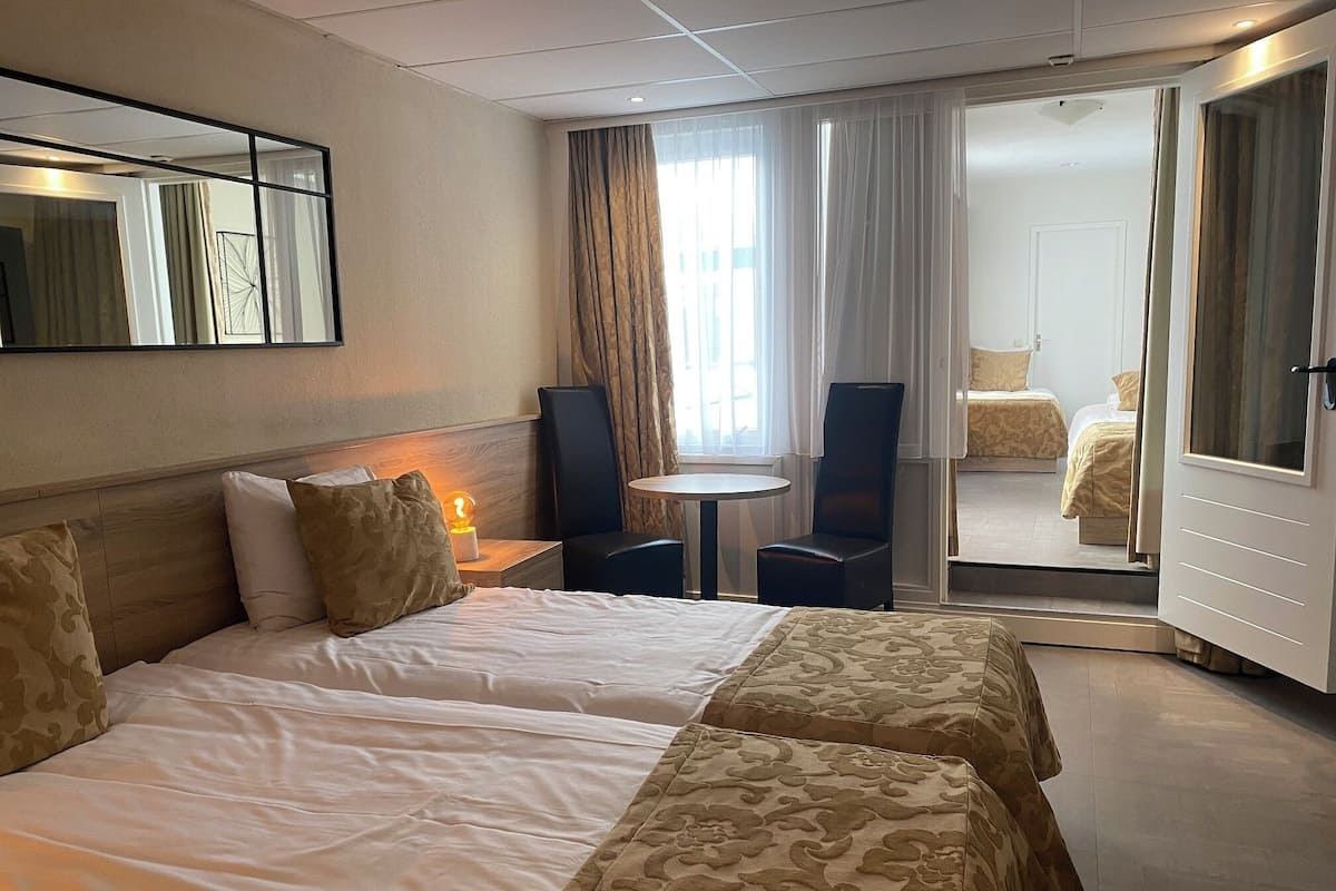 Ein Hotelzimmer mit zwei Betten, einem kleinen Tisch, einem Stuhl, einem Spiegel und einer Tür zu einem weiteren Raum.