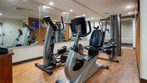 Academia com bicicletas ergométricas, esteira e parede com espelhos.