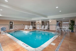 An indoor swimming pool with clear water, surrounded by lounge chairs and a tiled floor.