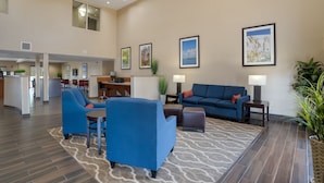Um hall amplo com um sofá azul, poltronas e uma área de refeições ao fundo.