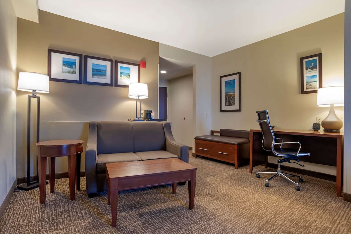 A hotel room with a sofa, a desk, a chair, a coffee table, and framed pictures on the wall.