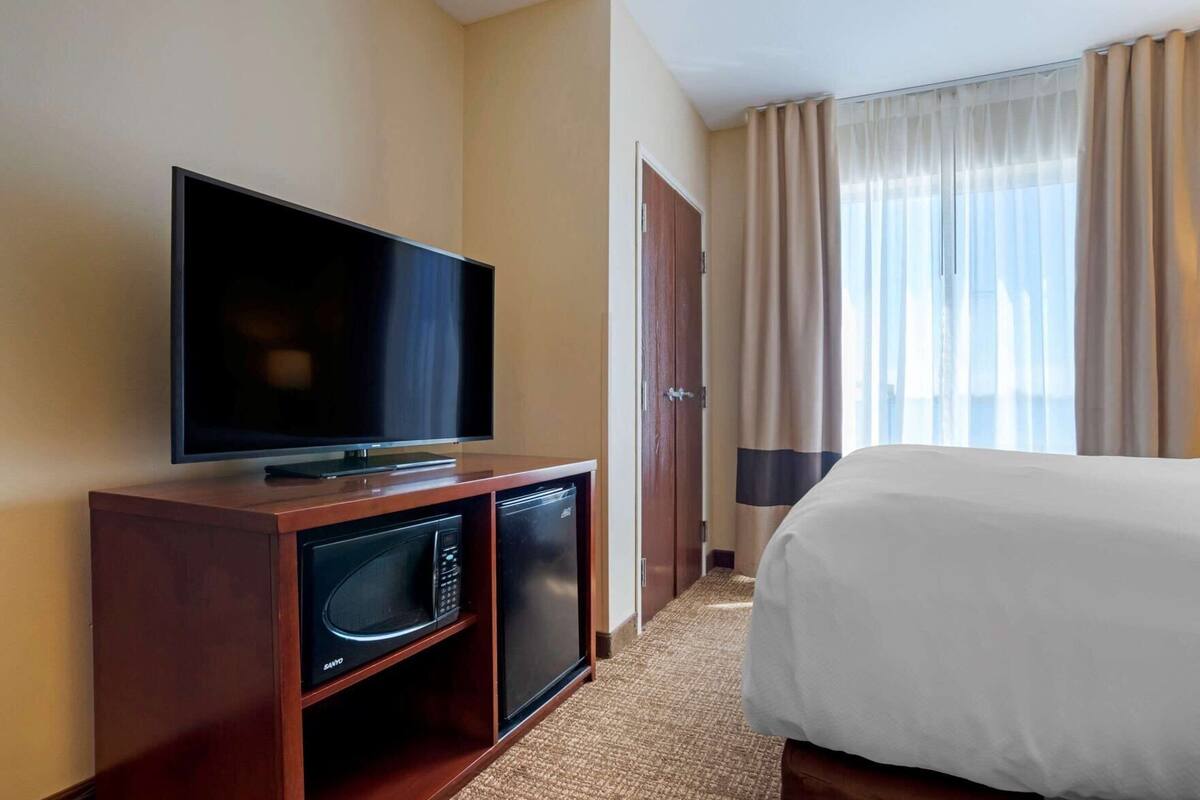 A hotel room with a flat-screen TV, a microwave, a bed, and a door leading to another room.