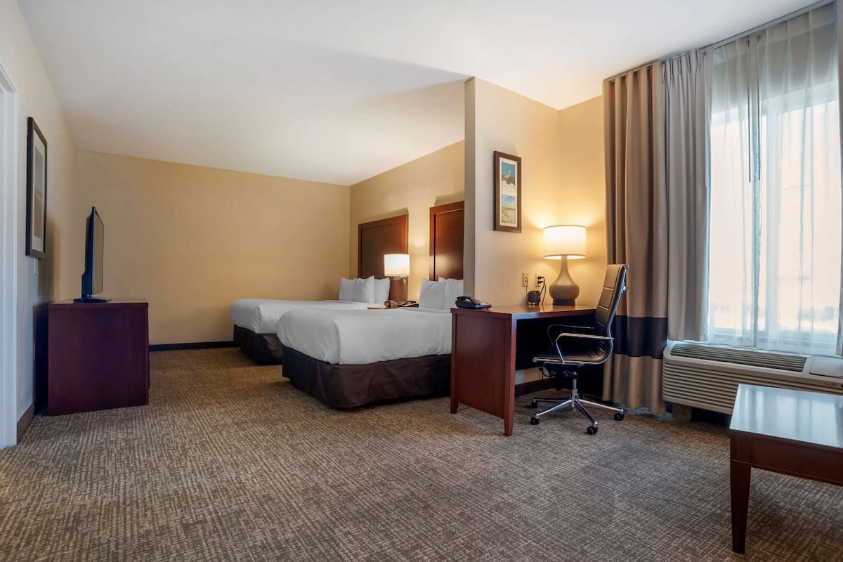 A hotel room with a bed, desk, chair, and a large window with curtains.