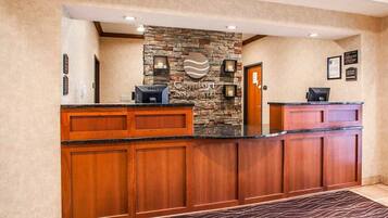A hotel reception area with a stone wall, wooden reception desk, and a welcome mat.