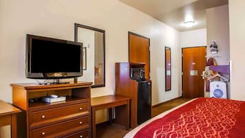 A hotel room with a bed, a television, a dresser, a microwave, and a coat rack.