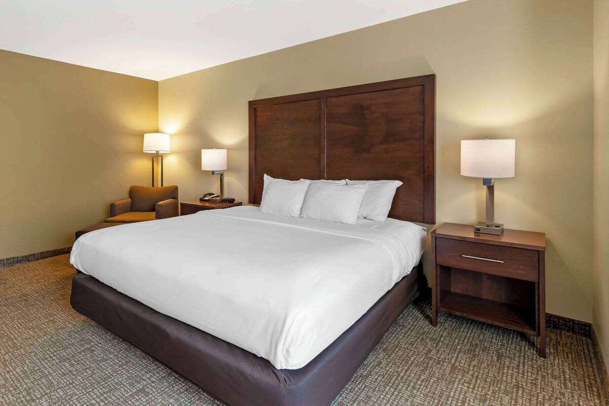 A hotel room with a large bed, two bedside tables with lamps, a chair, and a carpeted floor.