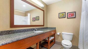 Un bagno con un top in granito, un vano contenitore in legno, un water bianco e una tenda da doccia.