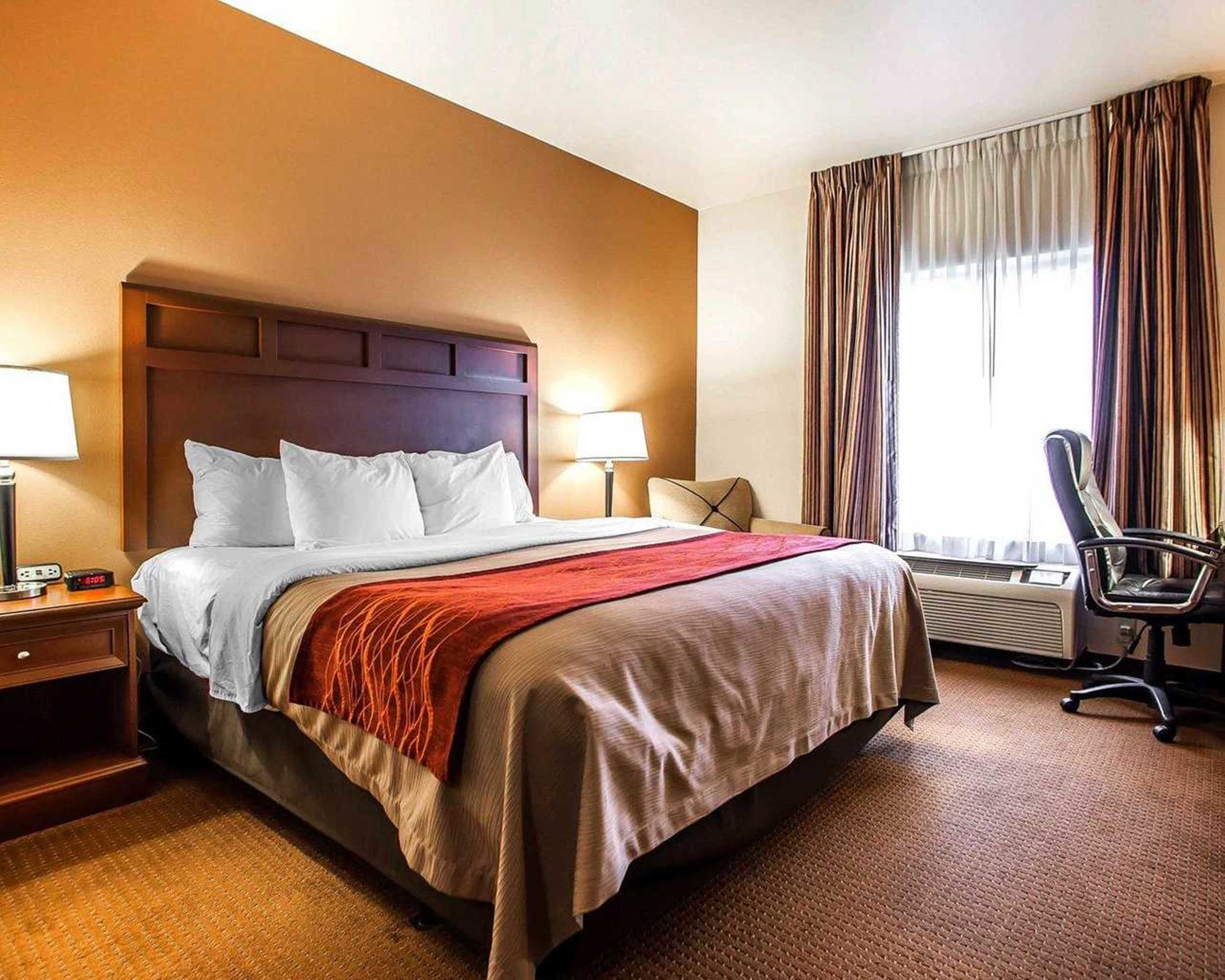 A hotel room with a large bed, two bedside tables with lamps, a chair, and a window with curtains.