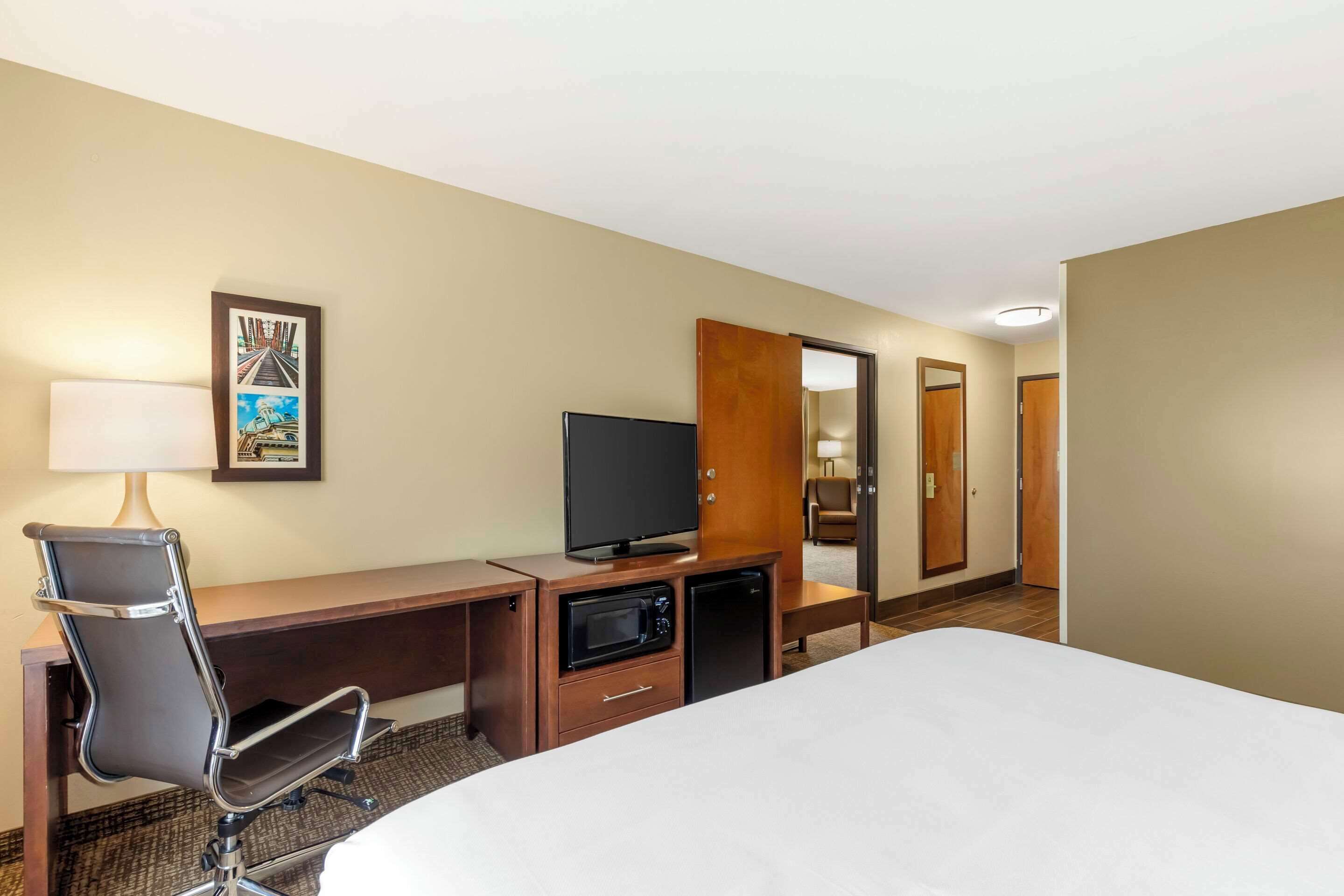 Een hotelkamer met een bed, een bureau met een televisie, een magnetron en een stoel.
