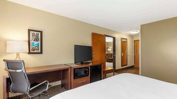 Een hotelkamer met een bed, een bureau met een televisie, een magnetron en een stoel.
