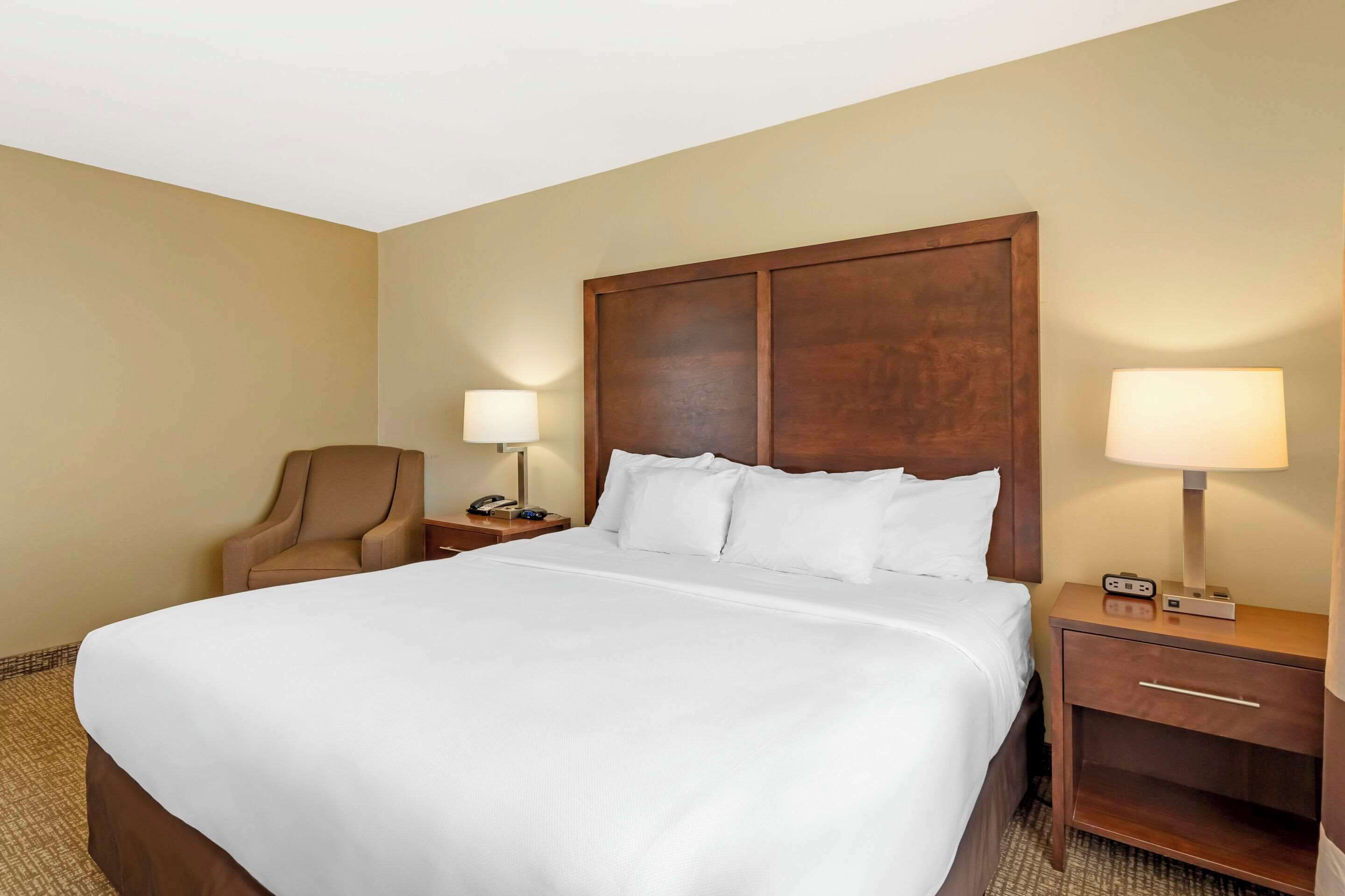 A hotel room with a large bed, two bedside tables, a chair, and a lamp.