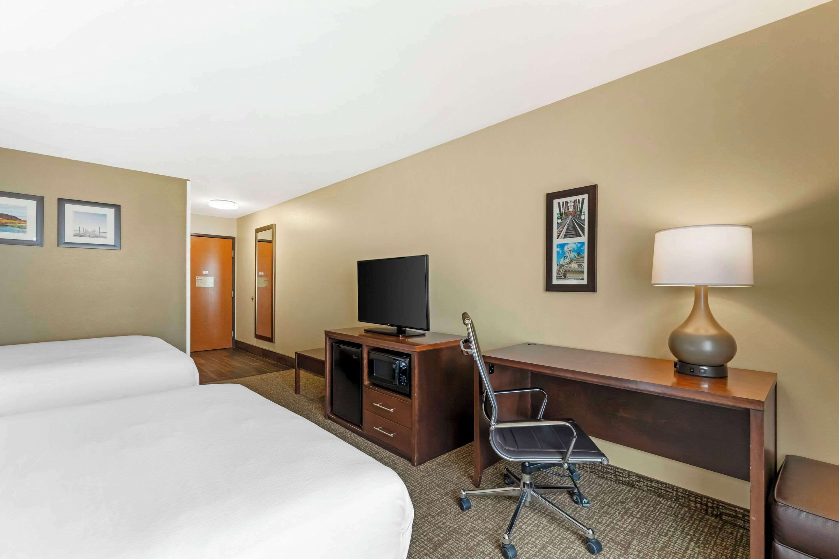 A hotel room with two beds, a desk with a television, a lamp, and a chair.