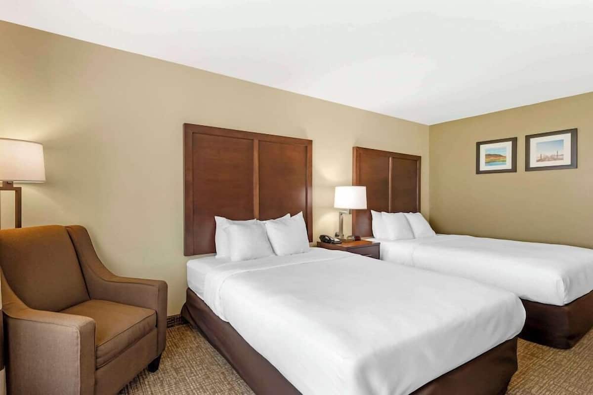 A hotel room with two beds, a chair, a lamp, and two framed pictures on the wall.