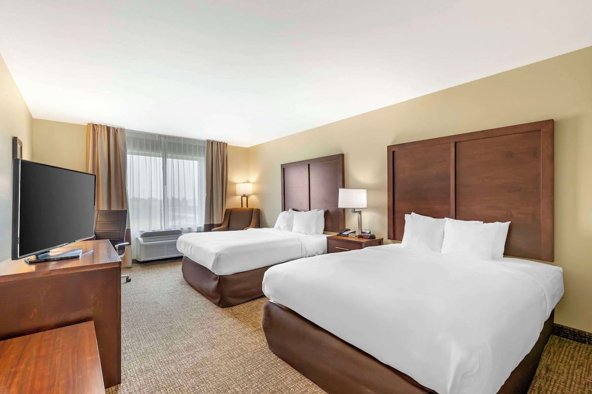 A hotel room with two beds, a desk, a TV, and a window with curtains.
