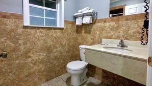A bathroom with a toilet, sink, and a window. - Budget Host Inn (Vernon)