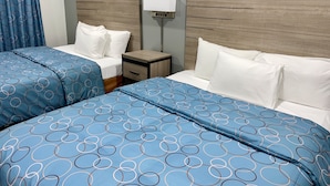 A hotel room with two beds, each with blue bedding and white pillows. There is a nightstand with a lamp between the beds. - Budget Host Inn (Vernon)