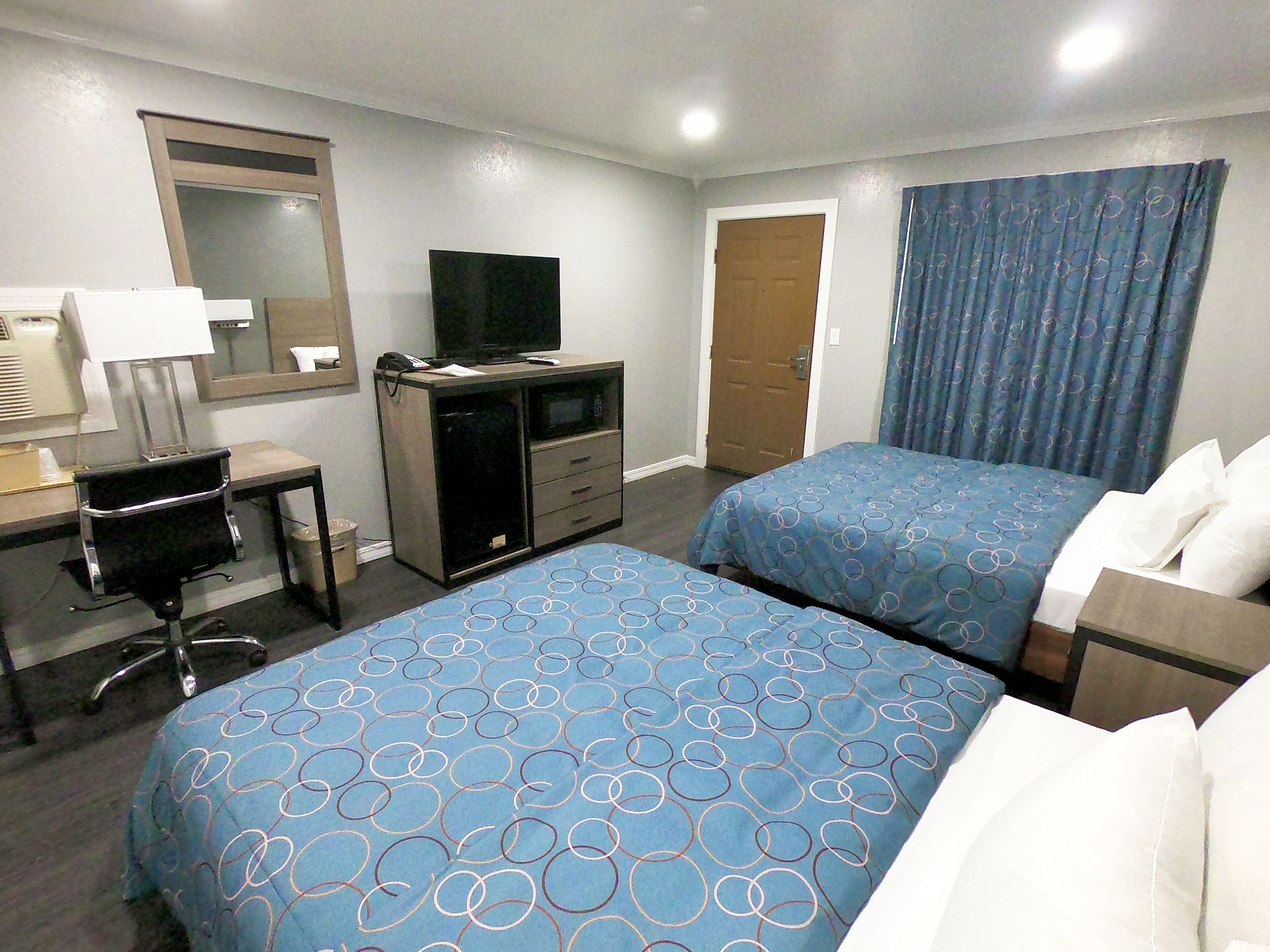 A hotel room with two beds, a desk with a computer, a TV, and a bathroom door.