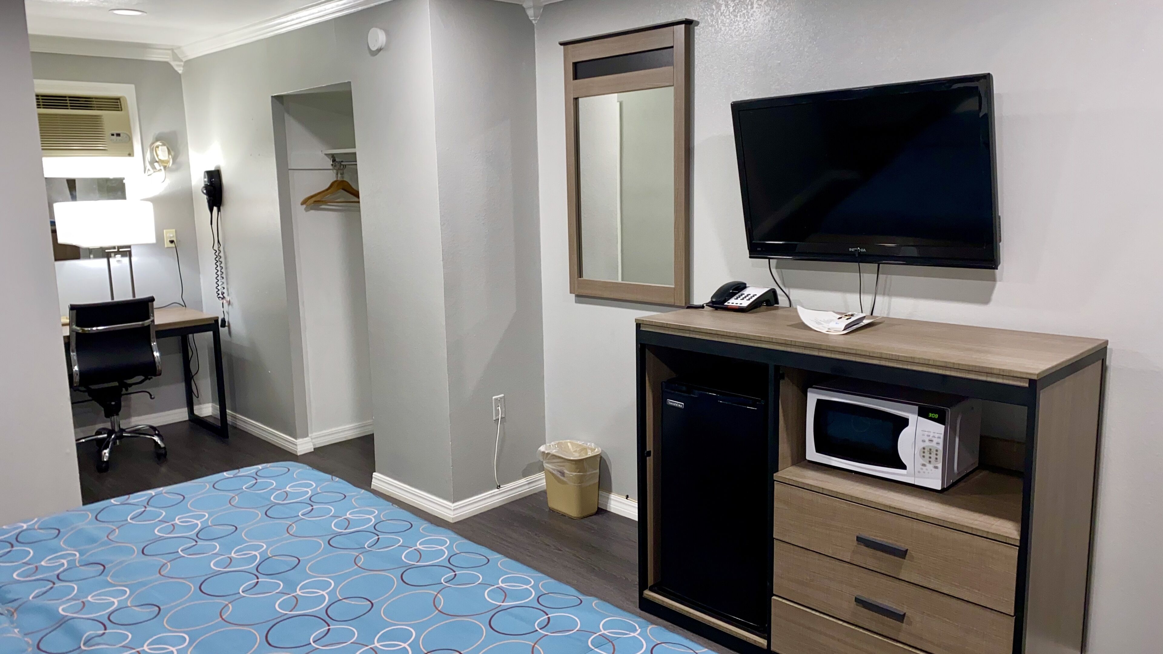 Une chambre d’hôtel comprenant un lit, un bureau avec une chaise, une télévision, un four à micro-ondes et un petit placard.
