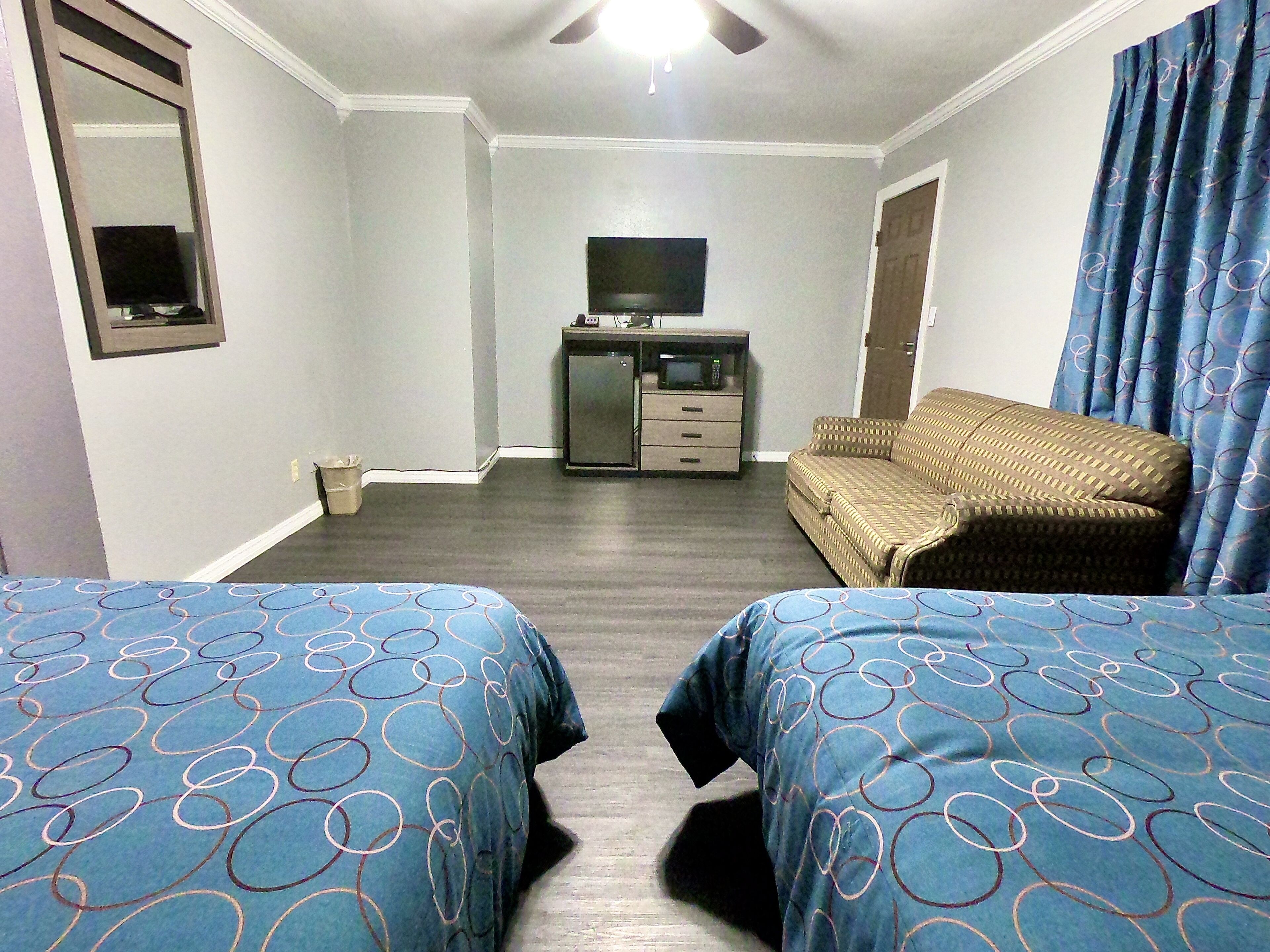 A hotel room with two beds, a television, a small cabinet, and a sofa.