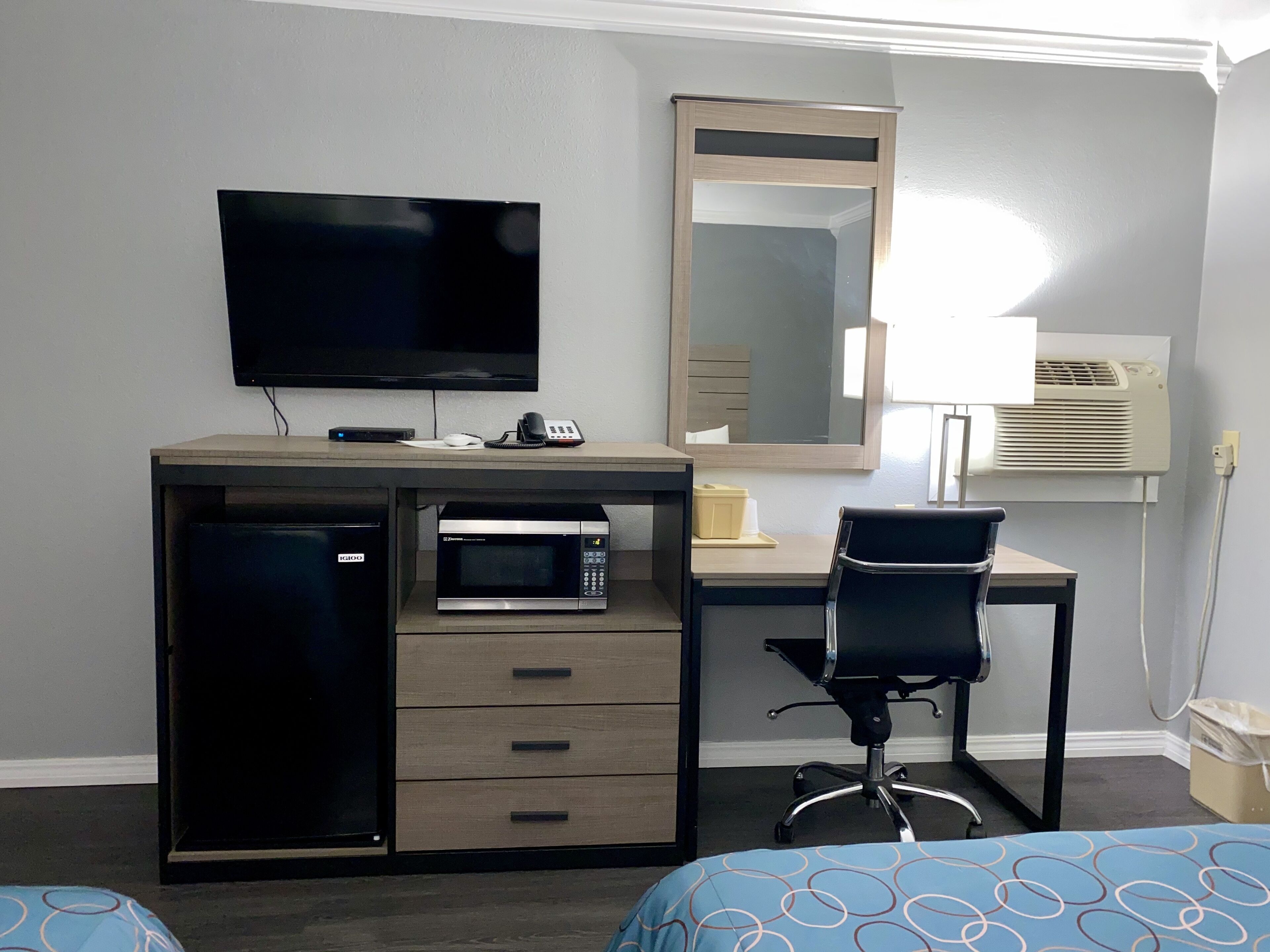 Una habitación de hotel con escritorio, televisión, microondas, silla y cama.