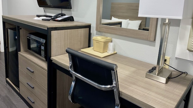 A hotel room with a desk, a chair, a microwave, a refrigerator, a telephone, a television, a bedside lamp, and a bedside table with a cup and a tissue box. - Budget Host Inn (Vernon)